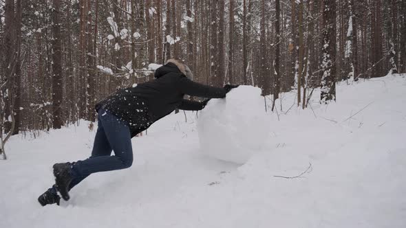 Caucasian Man Rolls Large Snow Globe with Effort alt