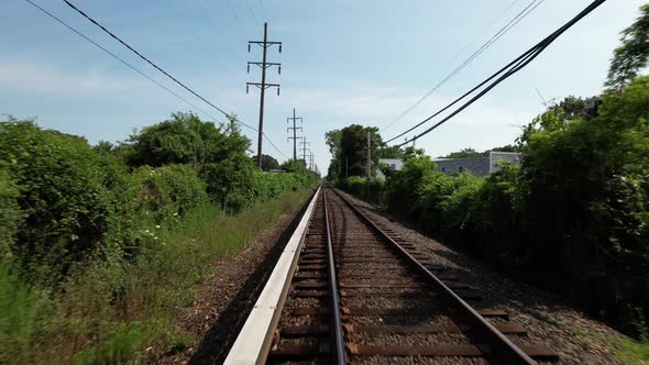 A low angle view looking straight down train tracks with green trees on either side. It runs through alt