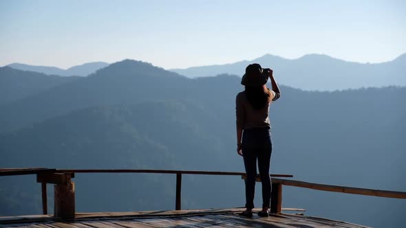 a female traveler standing on wooden balcony and looking at a beautiful mountain view