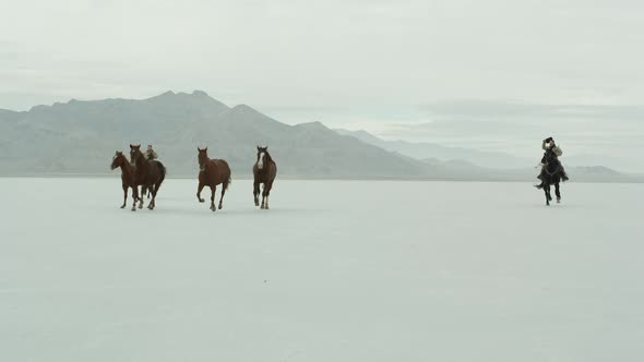 Horses running with cowboys riding across salt flats. alt