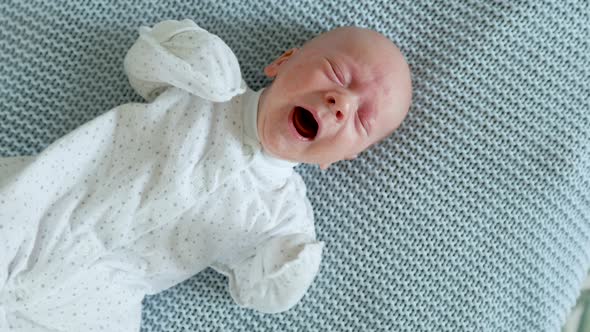 baby screams with his eyes closed while lying on the bed