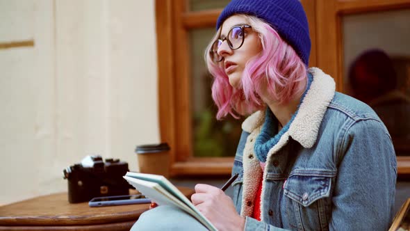 Cheerful woman in hat looking at the top and drawing in cafe alt
