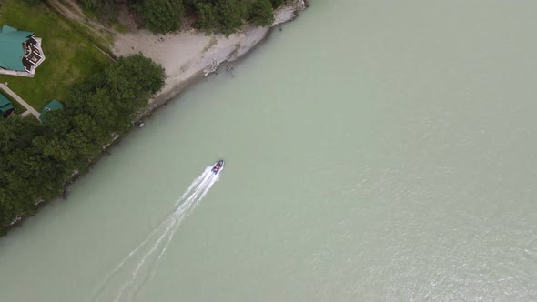 A Blue Inflatable Boat with Passengers is Dusting Along the Sandy Shore with Green Trees alt
