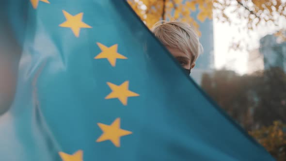 Young Caucasian Short Haired Woman with Face Mask Spinning in the Park with the European Union Flag alt