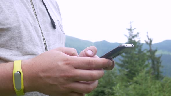 Unrecognizable Male Hands Using Smartphone on Mountain Forest Background