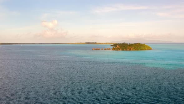 drone flight over the ocean in front of Bora Bora. Different blues in the water, small Motu / Island alt