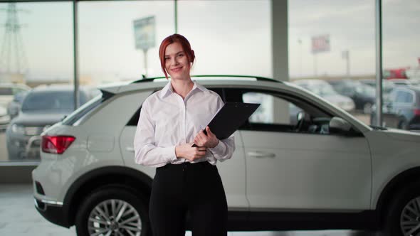 Portrait of Auto Sales Female Manager Holding Keys in Front of a New Car Smiling and Looking at alt