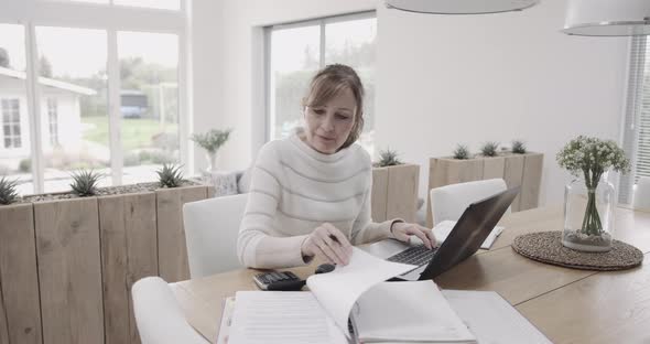 Senior adult woman doing domestic finance on laptop at kitchen table, day in life