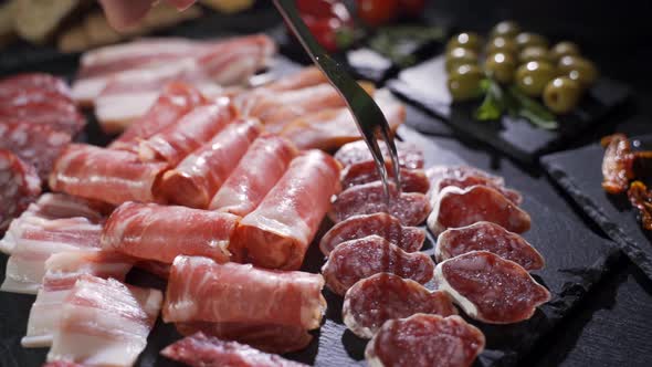 Fork Takes a Piece of Uncooked Jerked Sausages From a Wooden Board alt