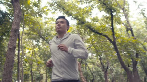 Young man athlete running in a public park and enjoying beautiful forests.