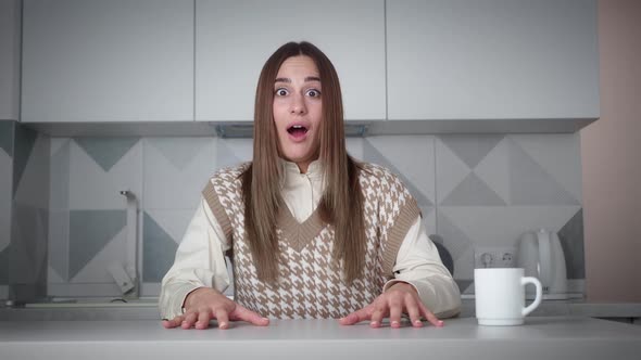 Excited Young Woman Winner Looks at Camera Celebrates Success Sits on Chair in the Kitchen alt