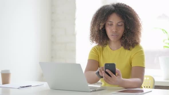 African Woman Browsing Internet on Smartphone while using Laptop in Office alt