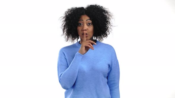 Smiling African Woman with Curly Hair Holding Finger on Her Lips Over White Background alt