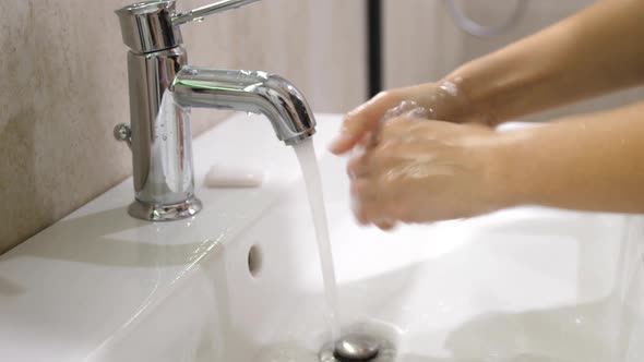 Hands of Woman Wash Their Hands in a Sink with Foam to Wash the Skin and Water Flows Through the