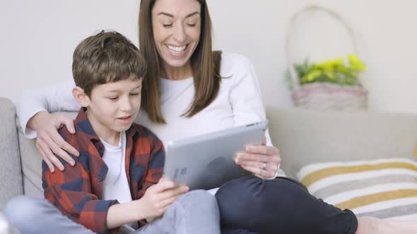 Mother and son sitting on couch using digital tablet