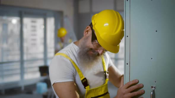 Tired Building Worker in Yellow Overall and Hardhat Standing and Leaning Head on Wall alt