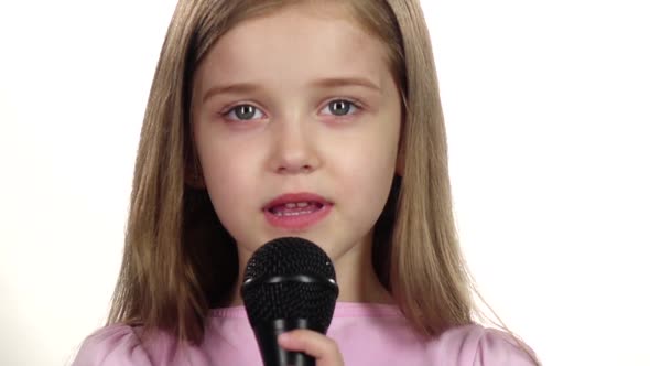 Child Girl Sings the Song Into the Microphone. White Background. Close Up. Slow Motion alt