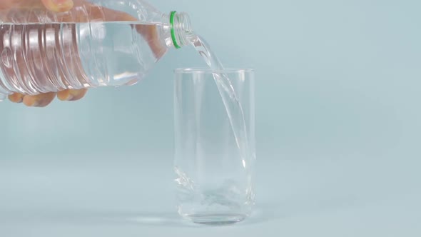 A hand puts water into a glass glass with a plastic bottle. alt