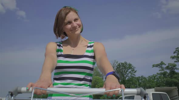 Young 30s woman spinning around holding shopping cart on outside car parking. alt