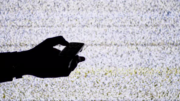 Silhouette of a Hand Holding a TV Remote on TV Screen Background with White Static Noise alt