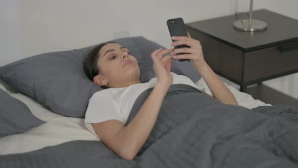 Hispanic Woman using Smartphone while Sleeping in Bed alt