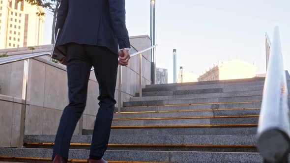 Unrecognizable Young Businessman Climbs Up Backlit Stone Stairs in City alt