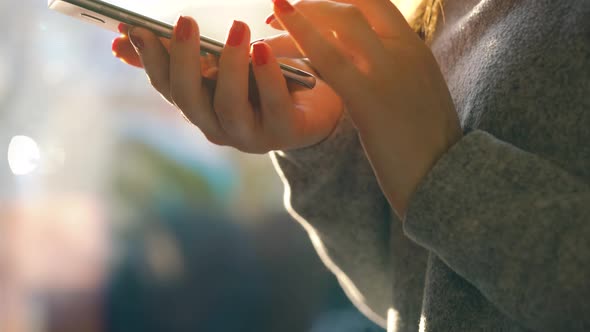 Female Hands Using Smartphone Against a Blurred Cityscape in the Setting Sun alt