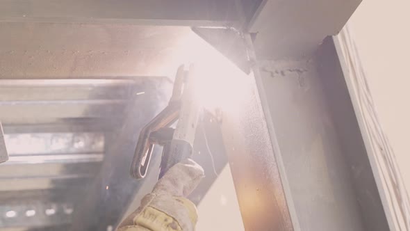 Sparks fly as welder wearing safety gloves weld steel structure; slowmo alt