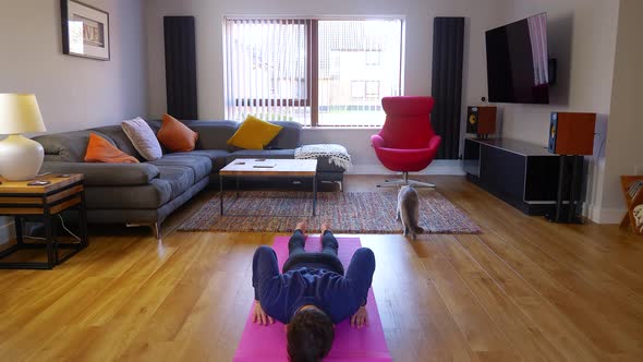 Young male doing home yoga exercise flow indoors, pet cat being inquisitive