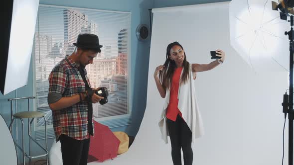 Pretty Black Model Making Selfie on Smartphone During Photo Shoot in Modern Studio alt