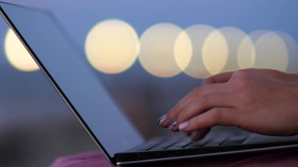 Female Hands Working on Laptop in the Evening Lights. alt
