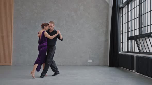 Man and Woman are Sensually Dancing a Tango in a Bright Hall with Large Windows