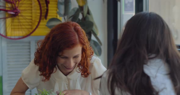 Two young business women colleagues laughing during a coffee break in a colorful boutique cafe. alt