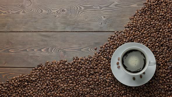 Black Frothy Coffee Spinning on Wooden Table Covered with Roasted Coffee Beans