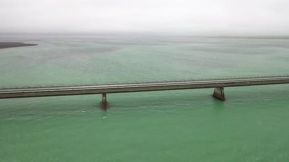 Bridge over water in Iceland with car driving with drone video pulling out. alt