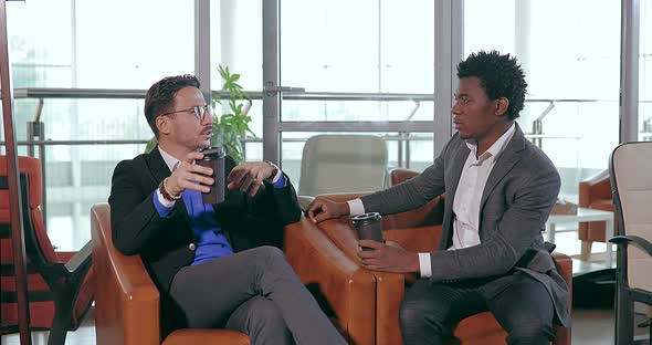 Businesspeople European and African Talking While Sitting in Chair in Office alt