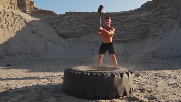 Muscle Athlete Strongman Man Hits a Hammer on a Huge Wheel in the Sandy Mountains in Slow Motion at alt