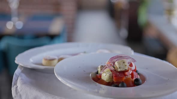 Closeup Greek Salad on White Plate on Tray in Hand of Unrecognizable Waiter Walking in Slow Motion alt