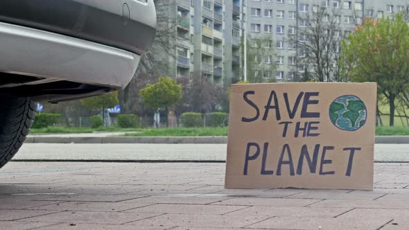 SAVE THE PLANET Poster Next to the Exhaust Pipe of a Car