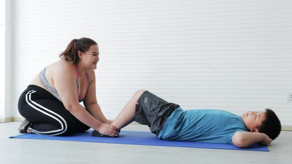 Overweight young woman in sportswear doing sit-ups with her son for the health care together