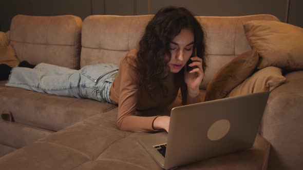 Young Woman Lying on Couch Talking on Phone While Using Laptop Lady Browsing Surfing Internet Social alt