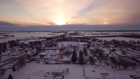 Aerial view flying backwards over a small town in the winter at sunset alt