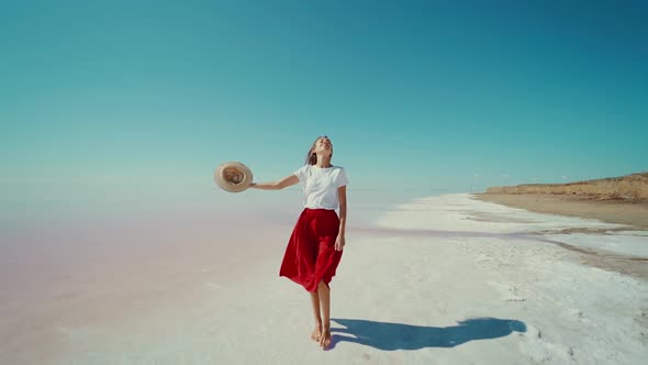 Elegant Traveler Woman Happy on Bright Pink Lake Salt Flats Girl with Hands Up alt