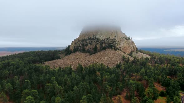 Drone footage of Devil's Tower rock surrounded by a dense forest in Wyoming, USA alt