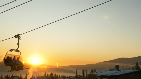 Skiers Sit on Modern Ski Lift and Move Over Resort Buildings alt