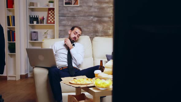 Man in Business Suit Working Late at Night on the Laptop in Front of His TV alt
