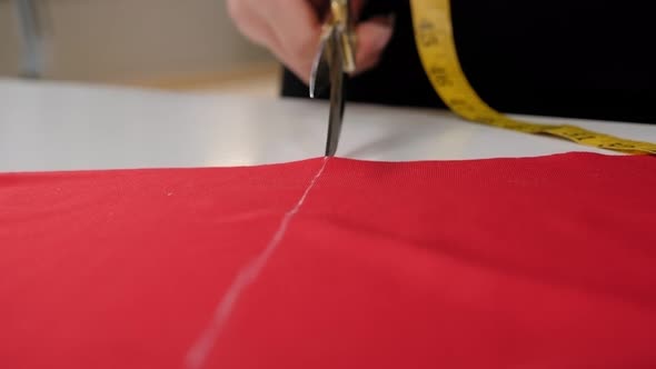 Closeup of a Seamstress Cutting a Red Fabric with Professional Metal Scissors alt