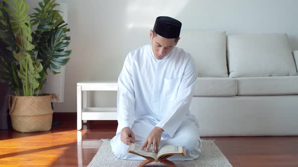 Young Muslim man wearing Islamic clothes reading the Quran