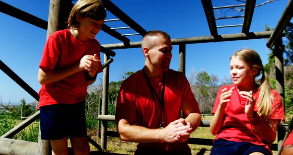 Trainer and kids relaxing during obstacle course training alt