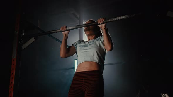 Girl Shakes Muscles and Pulls Herself Up on a Horizontal Bar in Gym alt